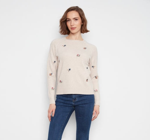 A cream-colored knit sweater with small embroidered floral motifs in blue, pink, and yellow, shown hanging on a rack.
