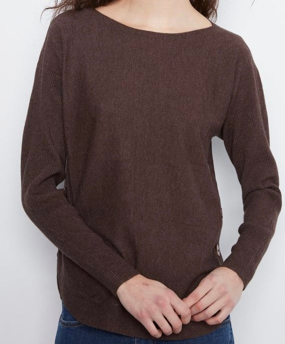 A woman wearing a dark brown long-sleeve knit sweater with a wide boat neckline, paired with blue jeans, shown from the chest down against a plain white background.