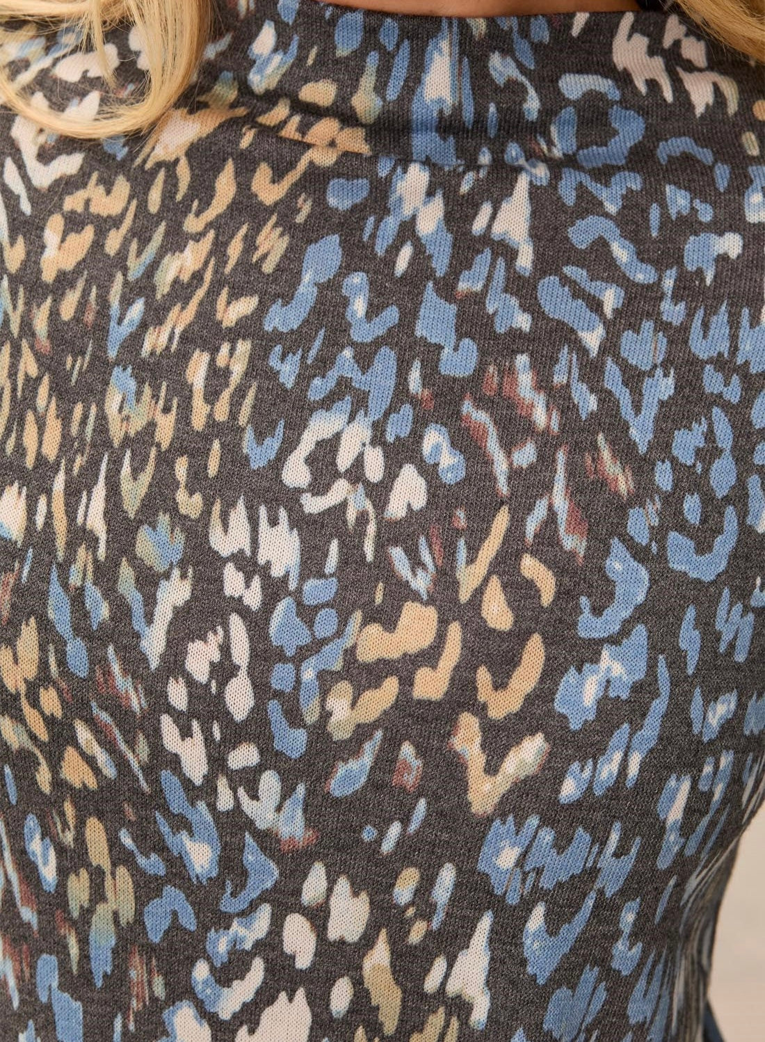 Close-up of a sleeveless top featuring an abstract leopard-like print in light blue, beige, and white on a dark charcoal gray background.