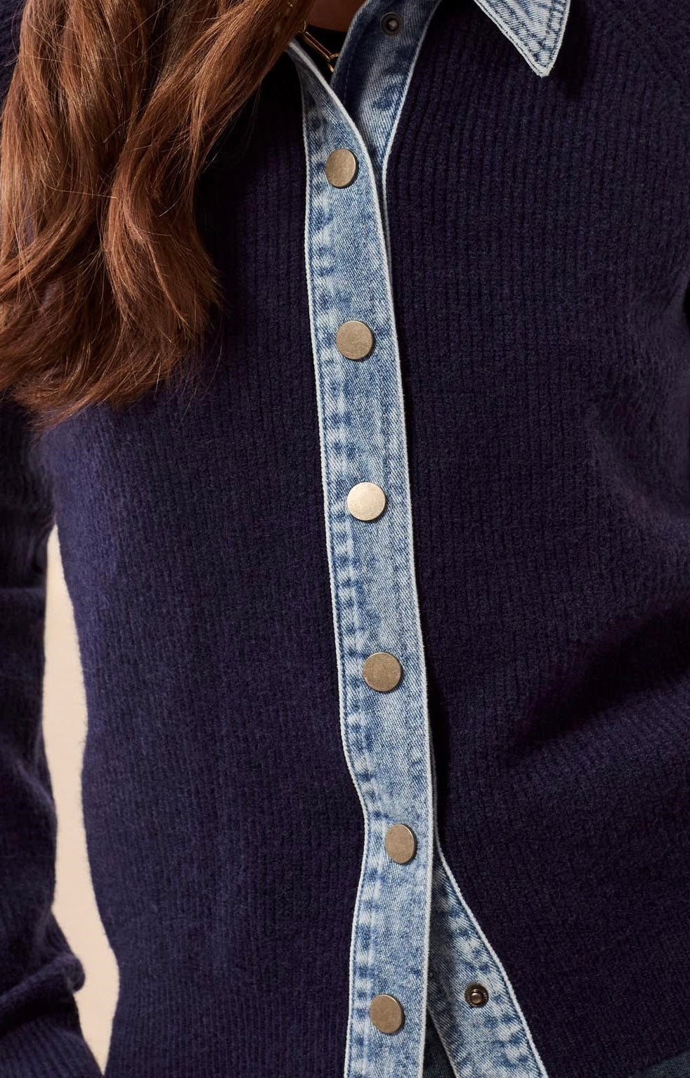 Close-up of a navy ribbed knit button-front top layered over a light blue denim shirt, with visible metal buttons and part of a person's brown hair.
