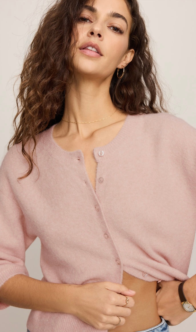 A woman wearing a light pink knit cardigan with a buttoned henley-style neckline, photographed against a plain light background.