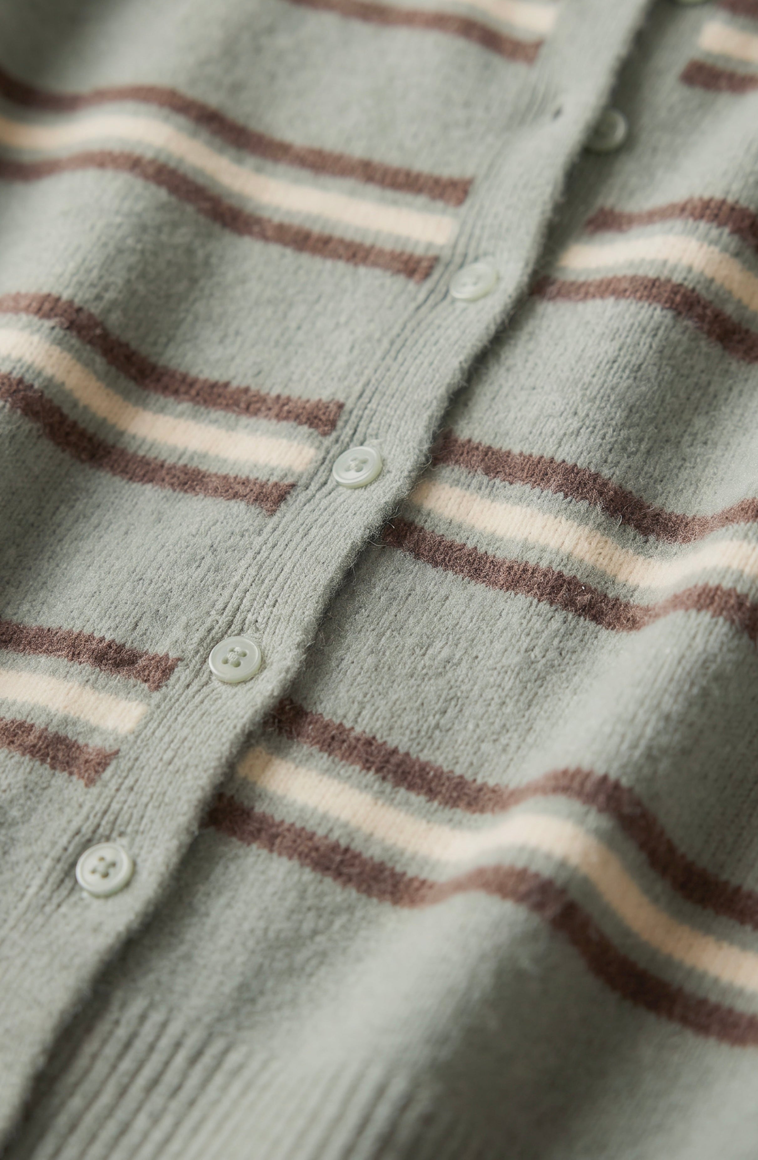 Close-up of a knit cardigan with horizontal stripes in sage green, brown, and cream, featuring a buttoned front closure.