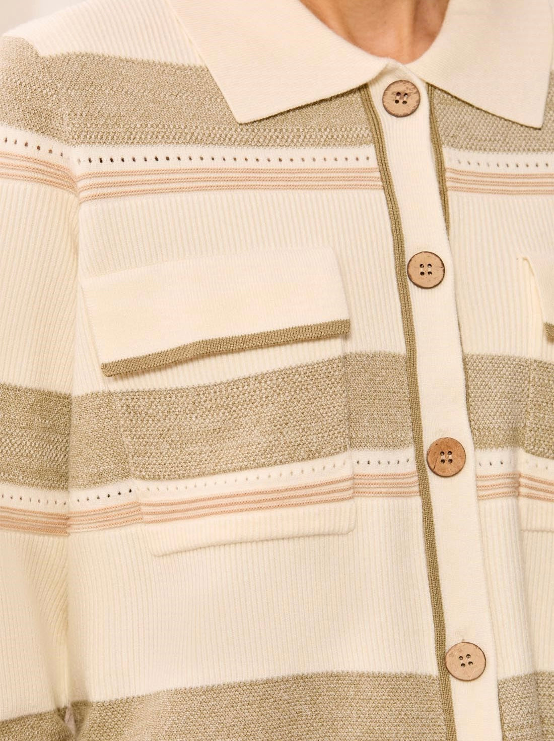 Close-up of a striped knit polo shirt with a cream collar and button placket, featuring horizontal stripes in cream, beige, and light brown, with matching wooden buttons.