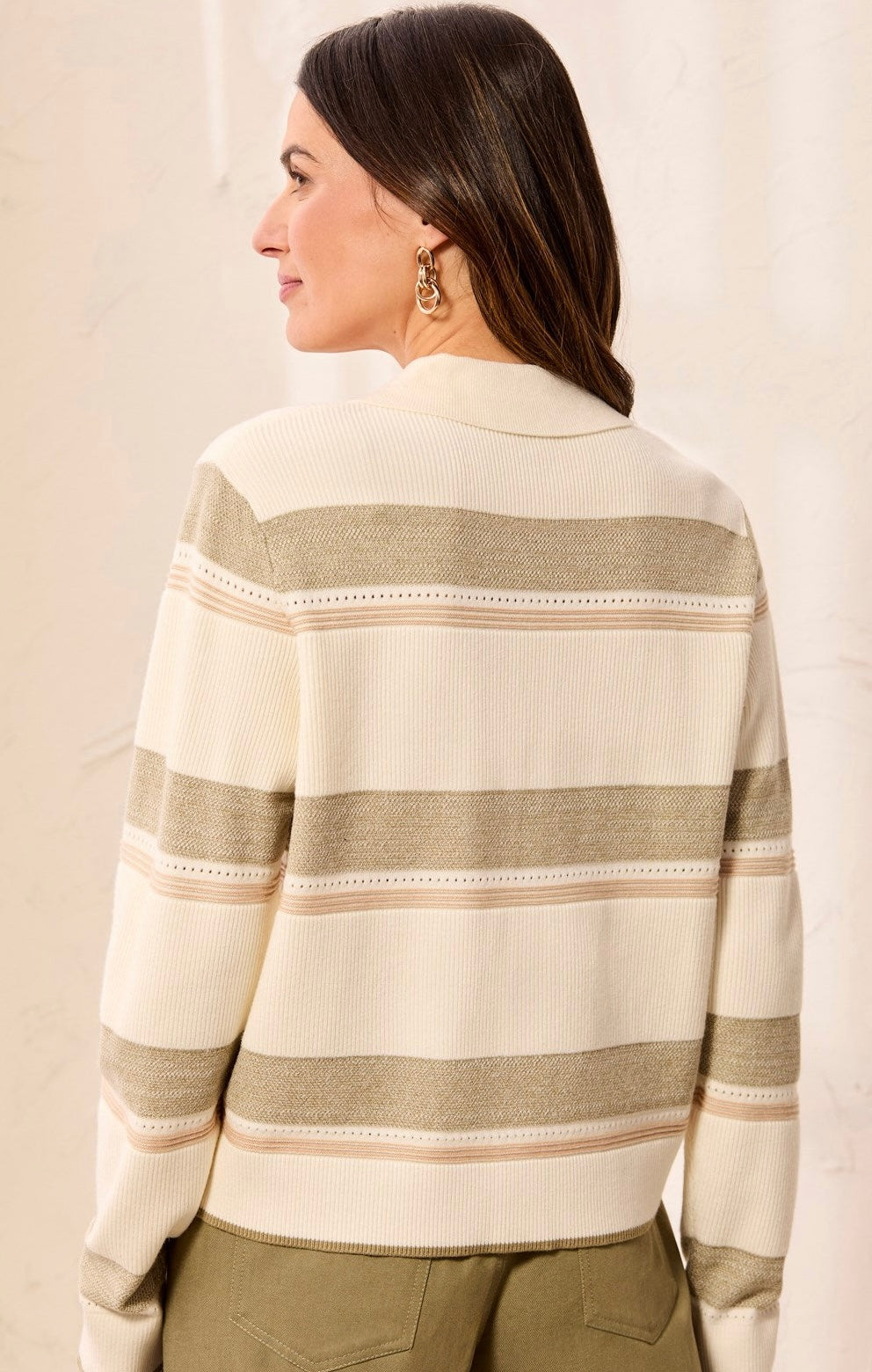 A woman shown from the back wearing a cream and beige horizontally striped knit sweater, paired with olive green pants, against a light beige textured background.