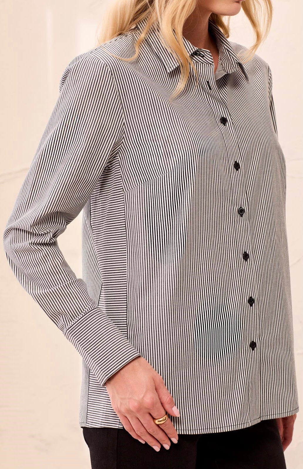 A woman wearing a long-sleeve button-up shirt with thin vertical black and white stripes, paired with black pants.