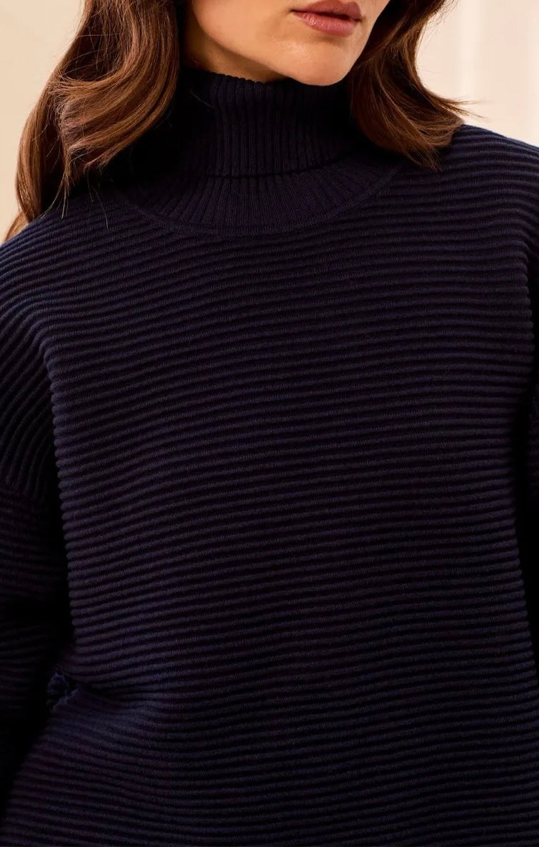 Close-up of a woman wearing a dark navy ribbed turtleneck sweater, showing the texture of the knit fabric and her brown hair.