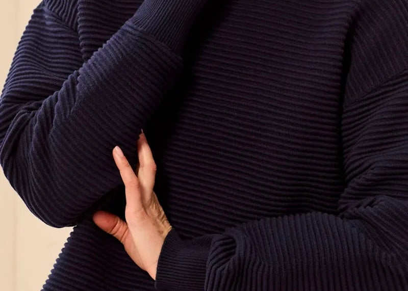 Close-up of a person wearing a dark navy ribbed knit sweater, showing the textured fabric and hand adjusting the sleeve.