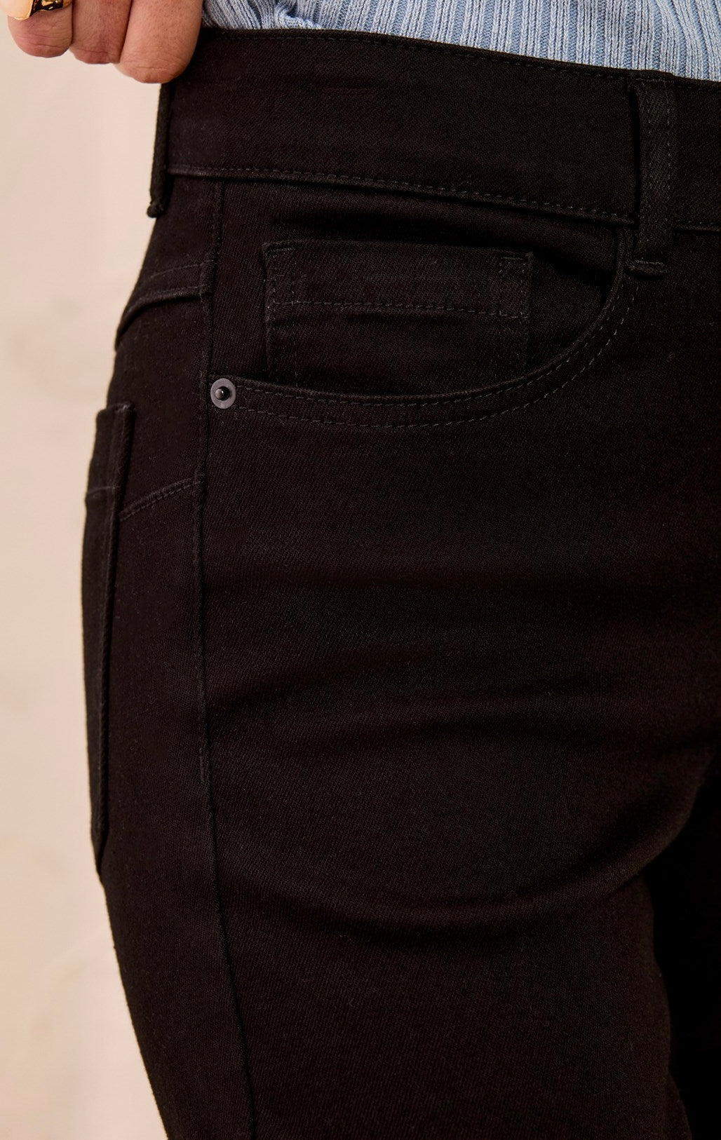 Close-up of a person wearing dark brown or very deep espresso jeans, showing the back pocket, waistband, and part of a light blue striped shirt.