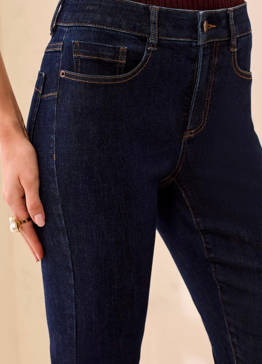 Close-up of a person wearing dark indigo blue denim jeans, showing the front pockets, waistband, and hand resting on the thigh.