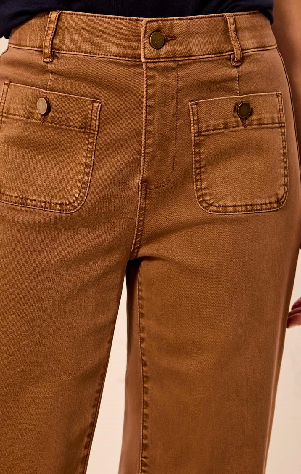 Close-up of the back waistband and pockets of brown denim jeans, showing a button closure and two back patch pockets.