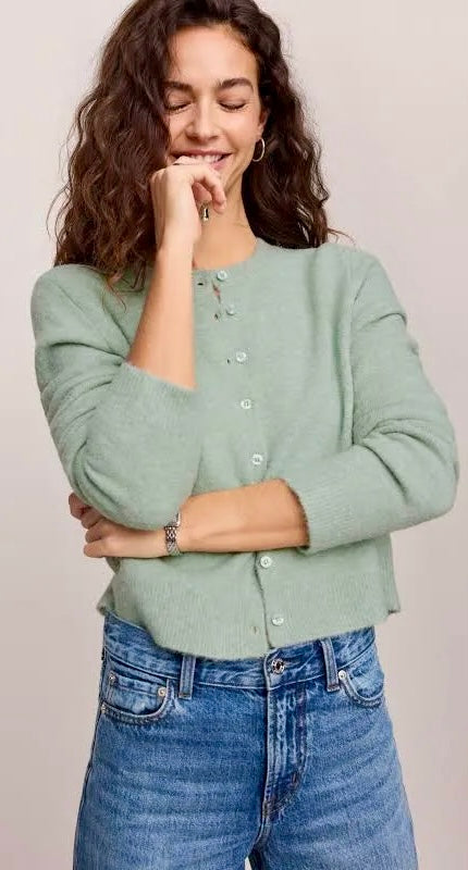 Woman wearing a light green long-sleeve shirt and blue jeans on a beige background