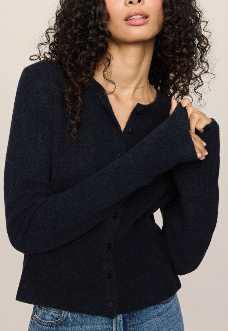 A woman wearing a dark navy blue knit cardigan sweater with a button-down front and ribbed trim, paired with blue jeans against a plain light beige background.