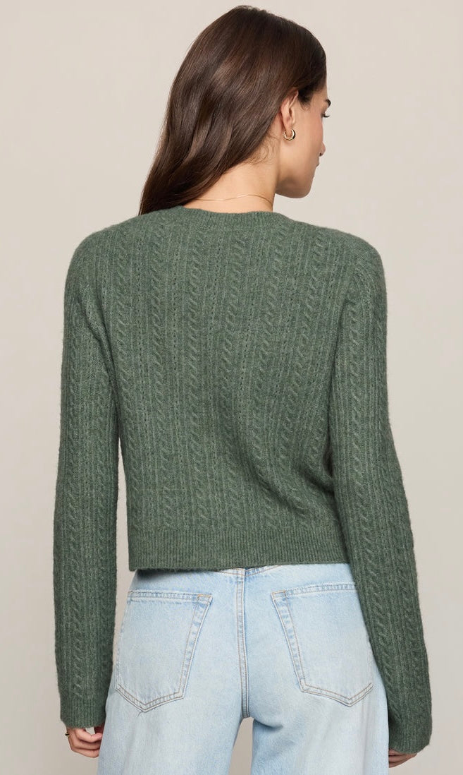 A woman shown from the back wearing a textured sage green cropped sweater and light blue jeans against a plain beige studio background.