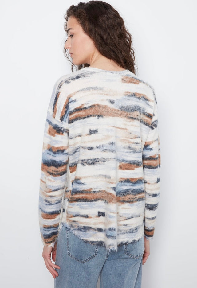 A woman shown from the back wearing a fuzzy long-sleeve sweater with horizontal watercolor-style stripes in cream, blue, brown, and gray, paired with light blue jeans against a plain white background.