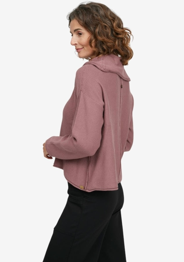 A woman wearing a dusty rose cropped hooded sweatshirt and black pants, shown from a side-back angle against a plain white studio background.