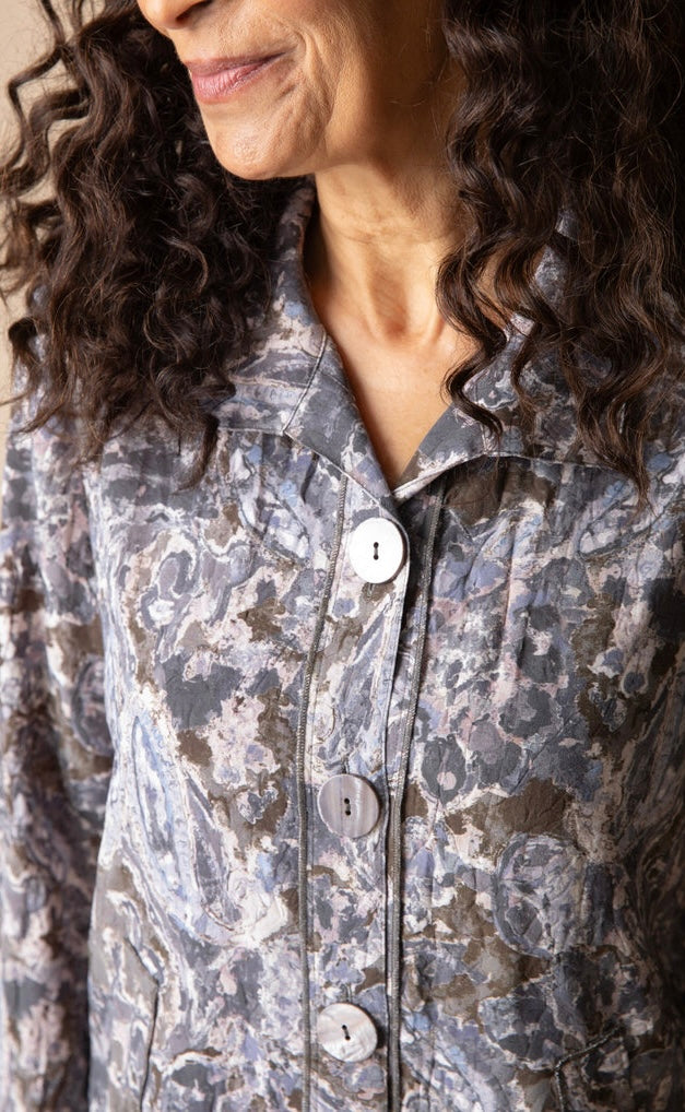 Close-up of a woman wearing a collared button-front jacket with a gray, blue, and beige abstract patterned fabric.