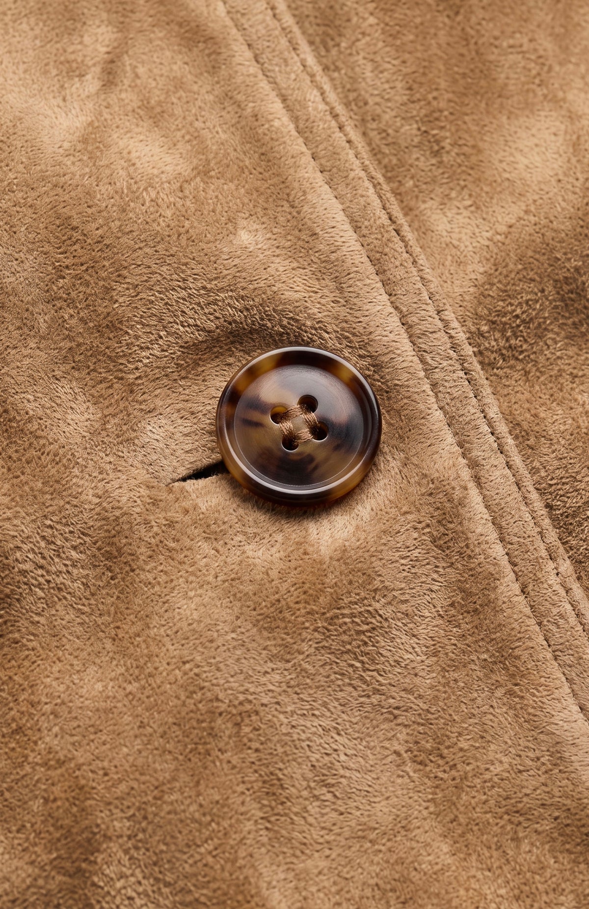 Close-up of a brown suede or microfiber fabric surface with a round four-button brown tortoiseshell-style button. -OLIVIA'S