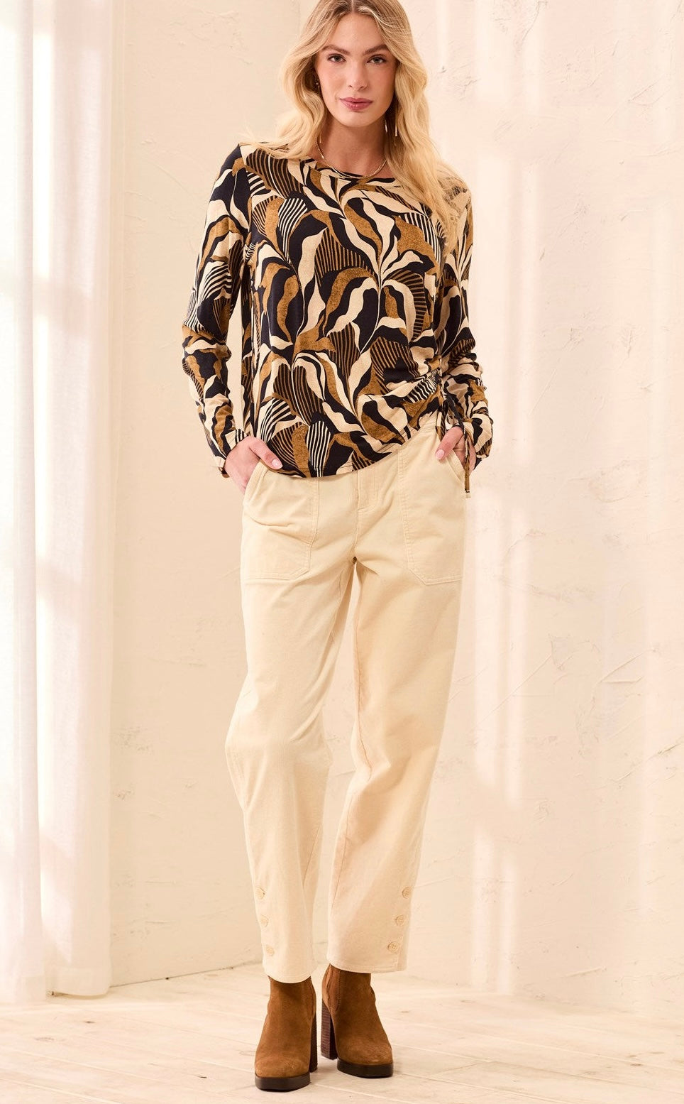 A long-sleeve knit top with a bold abstract botanical pattern in black, tan, and cream, held up on a hanger by a person in a clothing store.