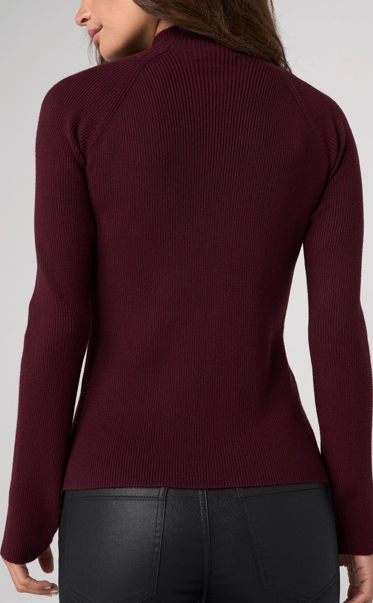 A woman wearing a ribbed long-sleeve mock neck sweater in deep burgundy, shown from the back against a light gray studio background.