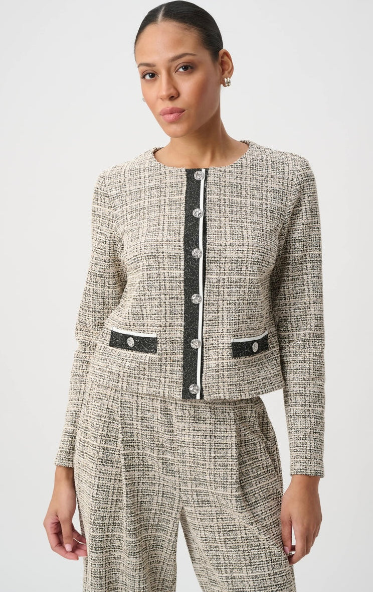 A woman modeling a matching tweed jacket and trousers set in a beige and black textured weave, featuring black trim and silver-tone buttons down the front and on the pockets.