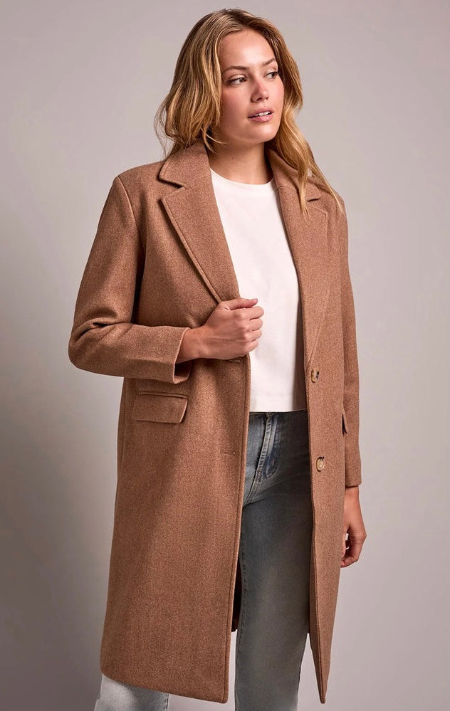 A woman modeling a mid-length camel brown wool-blend coat over a white top and blue jeans, photographed against a neutral light gray studio background. - OLIVIA'S