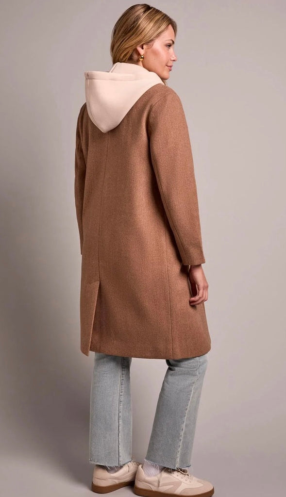 A woman shown from the back wearing a mid-length camel brown coat with a contrasting light beige hood, paired with light blue jeans and beige sneakers, against a neutral gray studio background. - OLIVIA'S