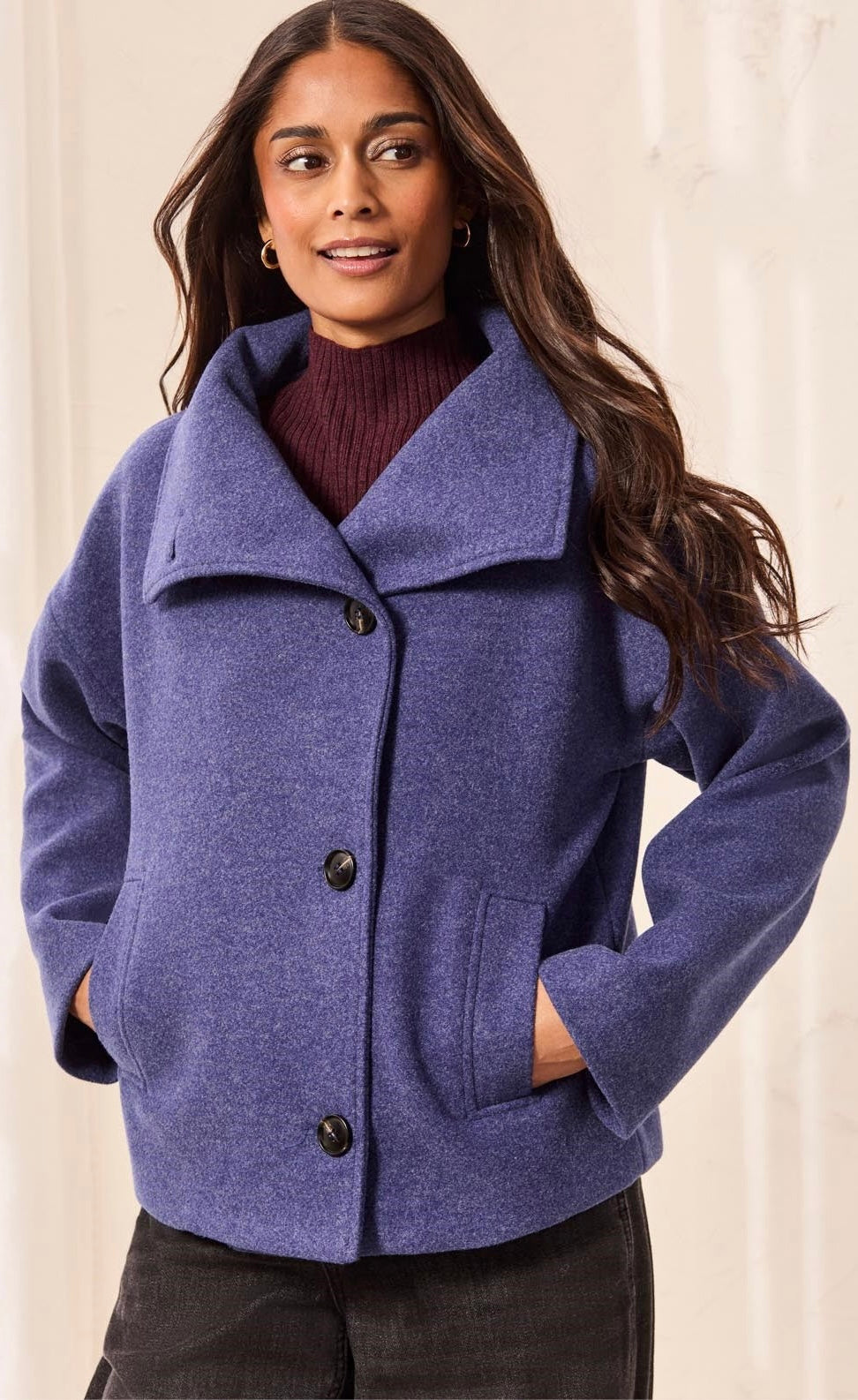 A woman wearing a heathered periwinkle blue wool-blend coat with a wide collar and three front buttons, layered over a burgundy ribbed turtleneck sweater and dark pants. - OLIVIA'S