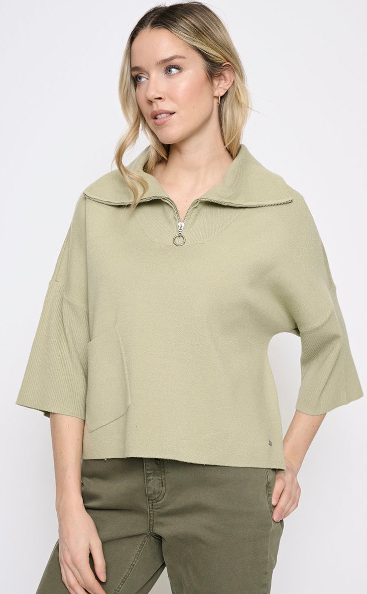 A woman wearing a sage green cropped quarter-zip pullover top with wide three-quarter sleeves and olive green pants, photographed against a light gray studio background. -OLIVIA'S