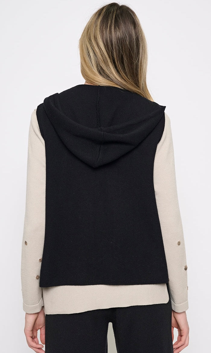 A woman shown from the back wearing a black hooded sleeveless vest layered over a beige and black long-sleeve top, against a plain white studio background. - OLIVIA'S