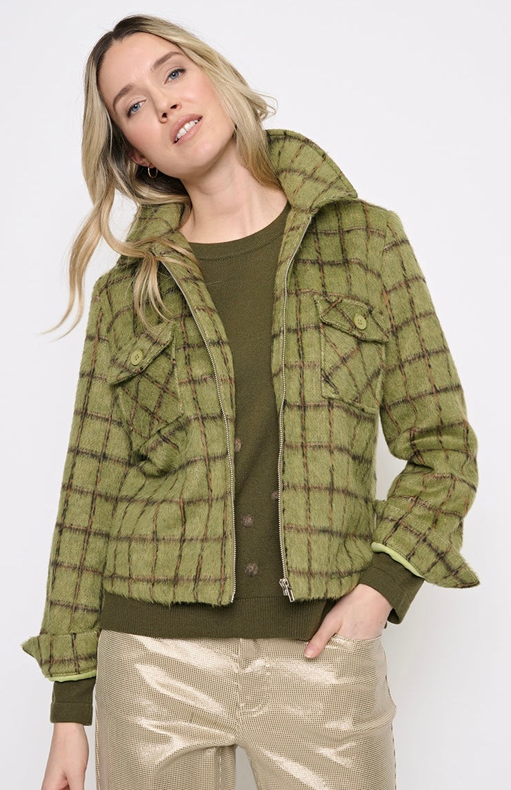 A woman wearing a cropped olive green plaid jacket over an olive green top and shiny beige pants, photographed against a plain light gray studio background. - OLIVIA'S