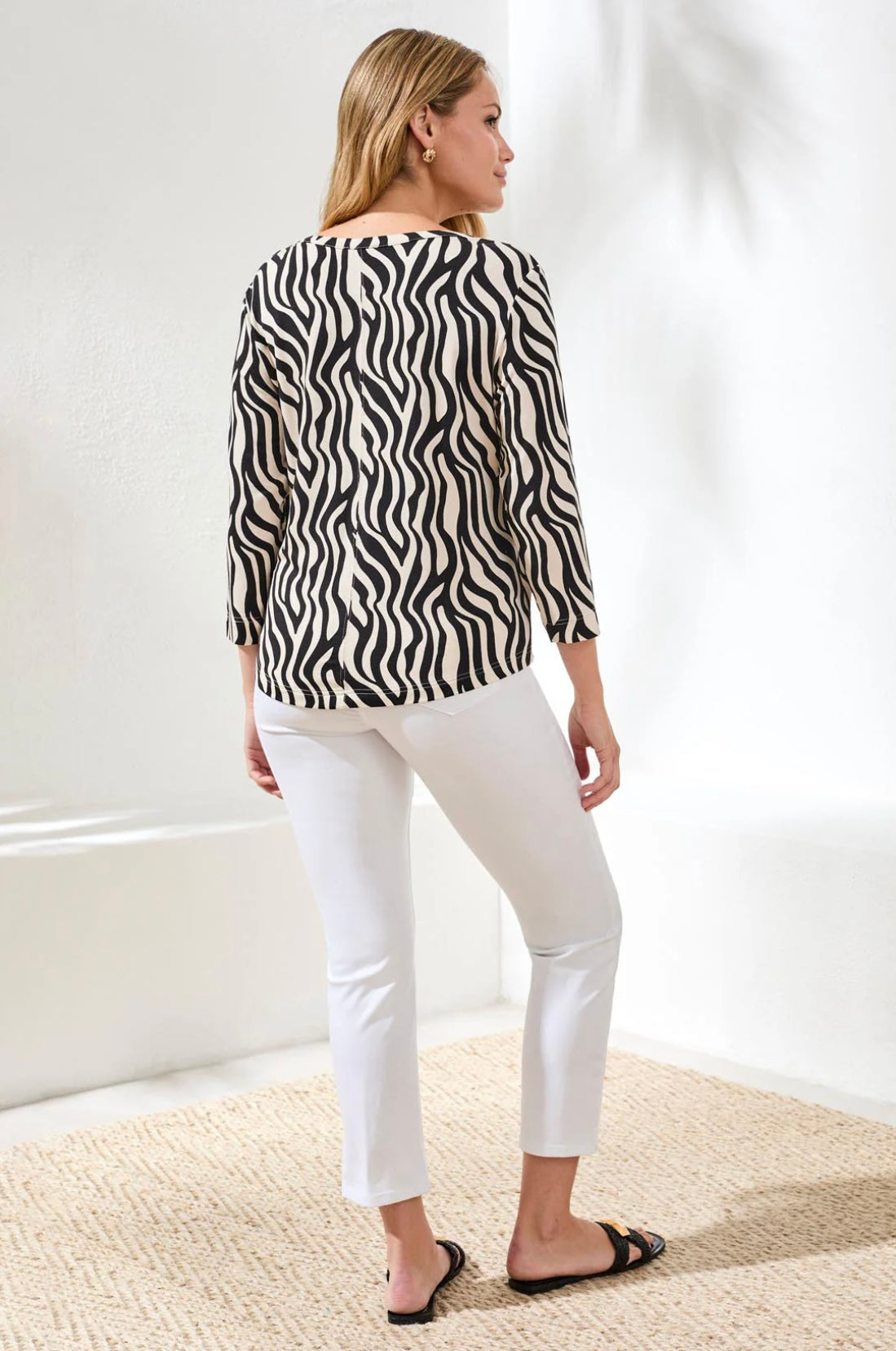 Woman wearing a zebra print top and white pants in a minimalistic setting