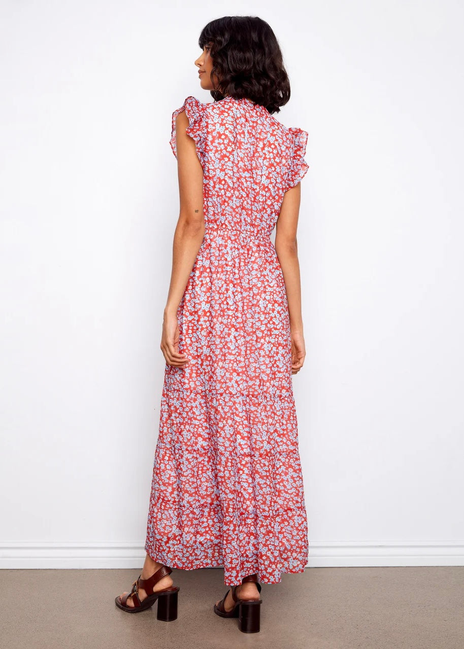 Woman wearing a floral dress standing against a white wall.