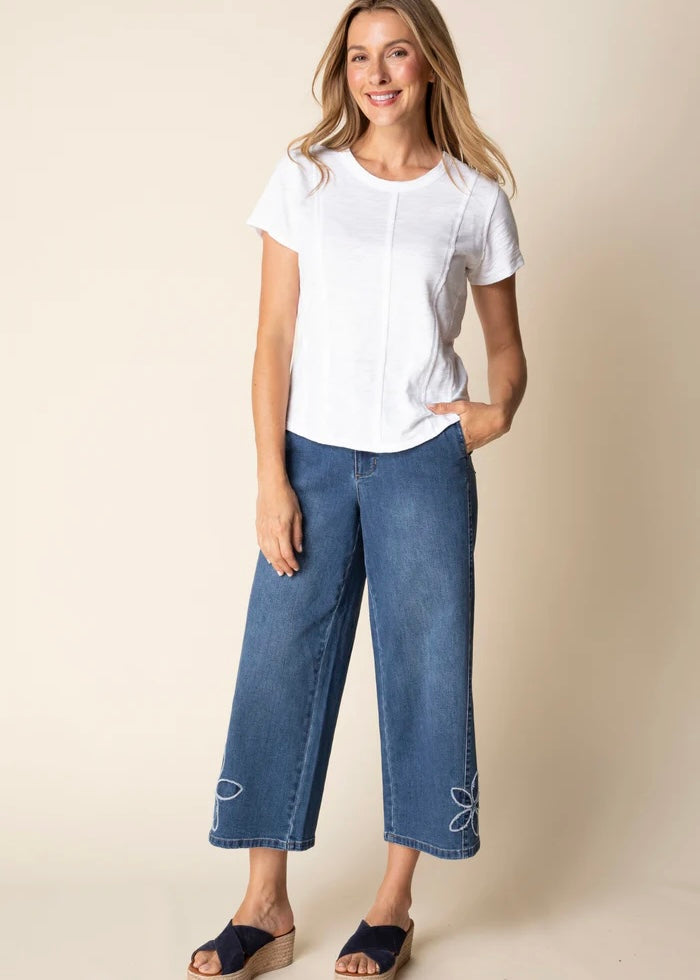Woman wearing a white top and blue jeans against a beige background