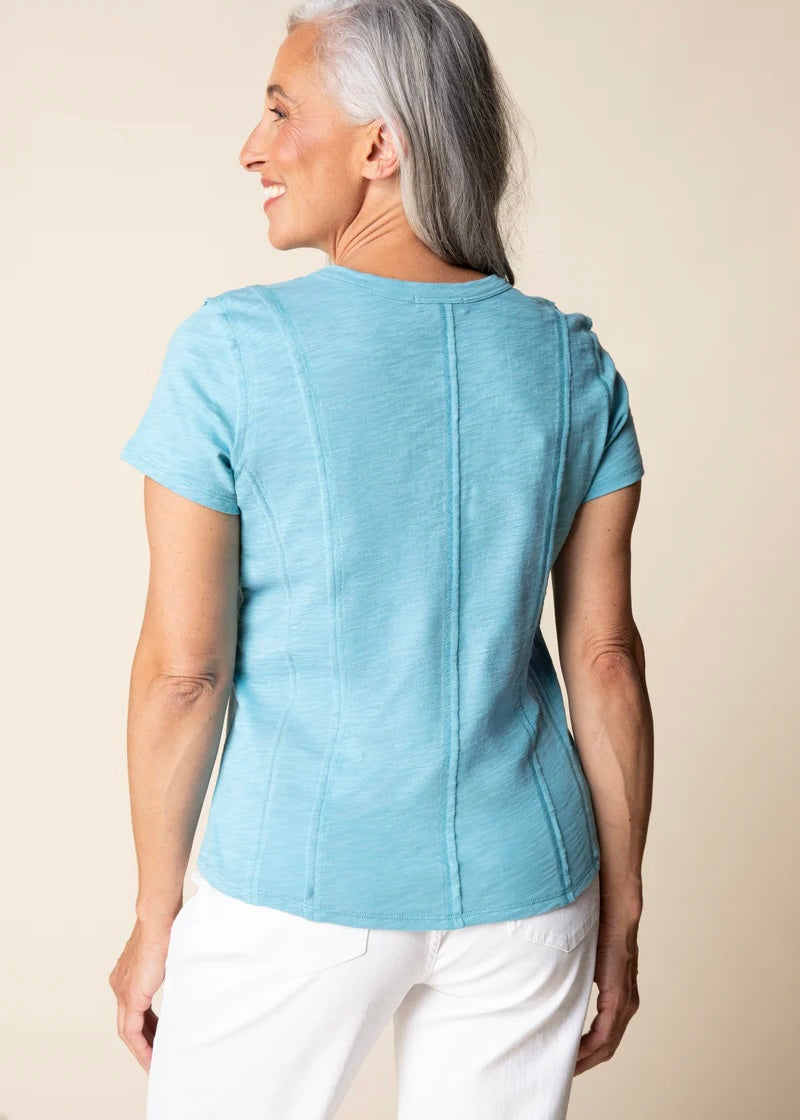 Woman wearing a light blue top and white pants against a beige background