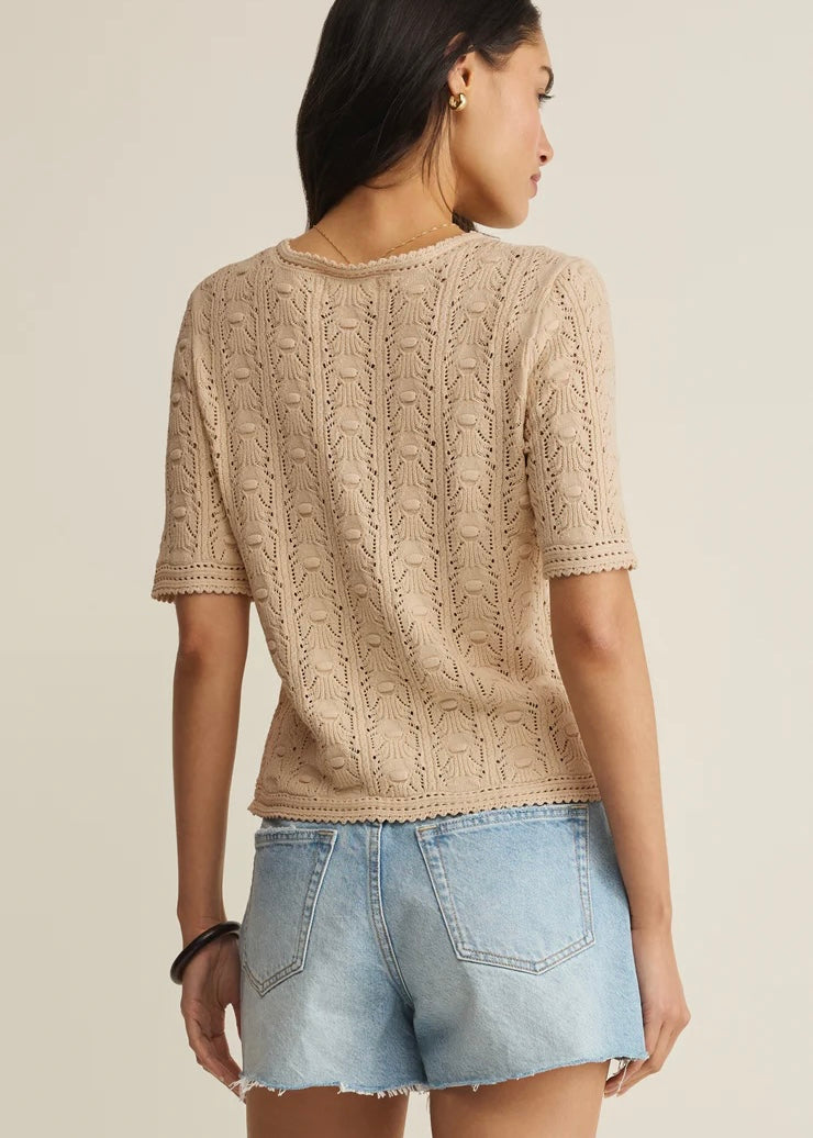 Woman wearing a beige knitted top and denim shorts on a plain background
