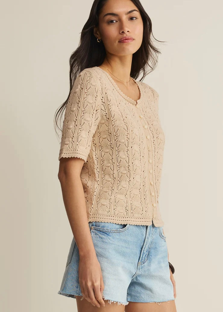 Woman wearing a beige lace top and denim shorts on a plain background