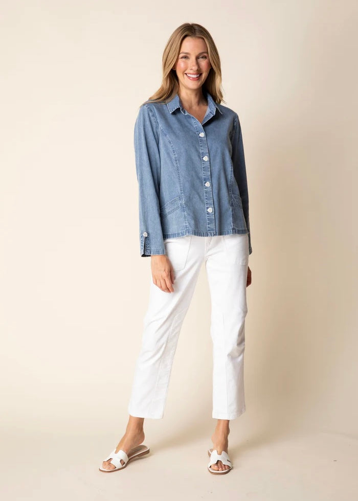 Woman wearing a blue denim shirt and white pants on a beige background