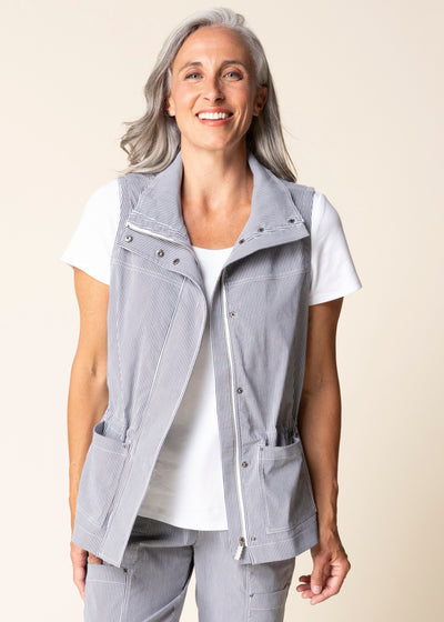 Woman wearing a light gray vest over a white shirt on a beige background