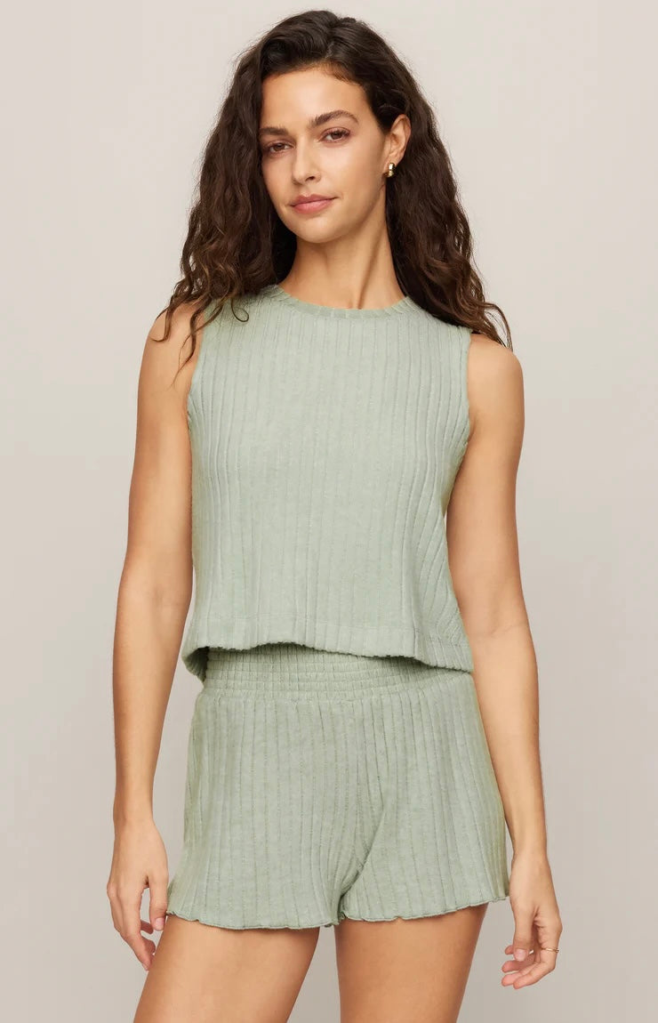 Woman wearing a green ribbed sleeveless top and shorts on a plain background