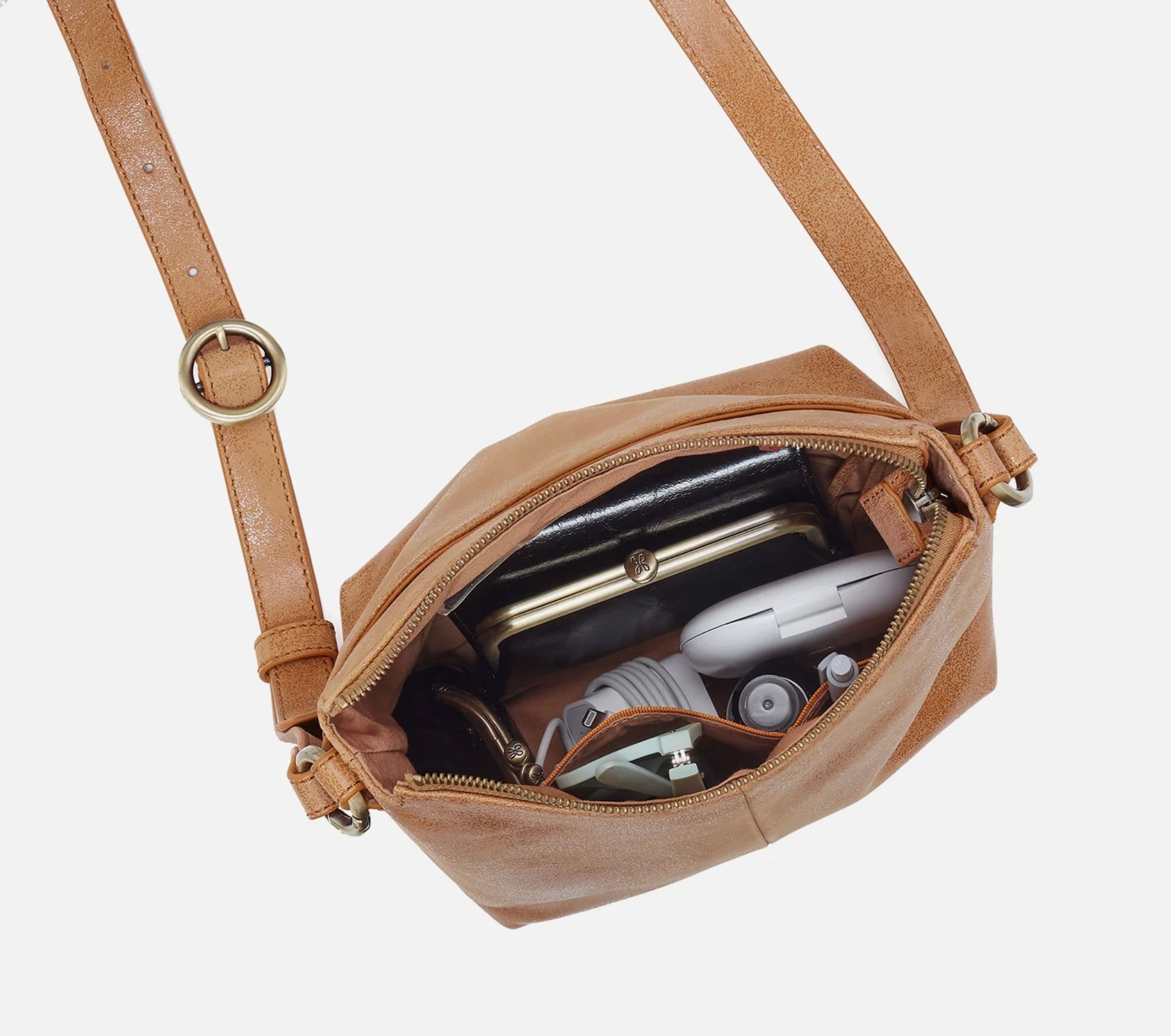 Brown leather crossbody bag with items inside on a white background