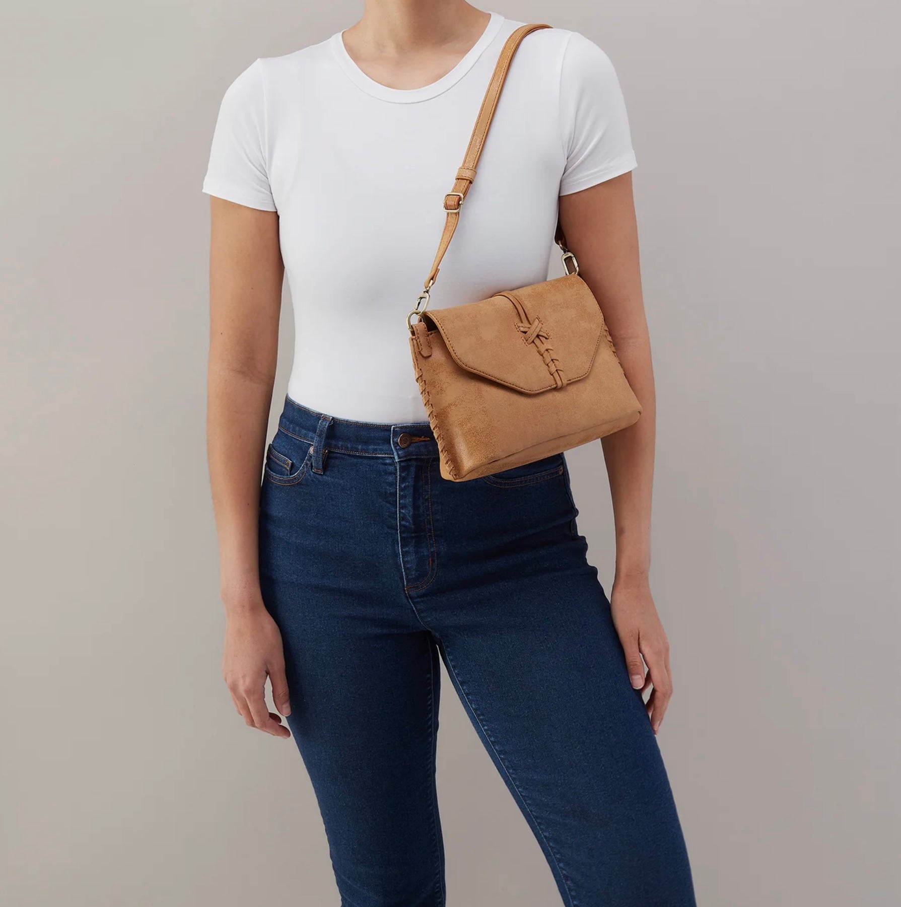 Person wearing a white t-shirt, blue jeans, and carrying a tan crossbody bag on a plain background