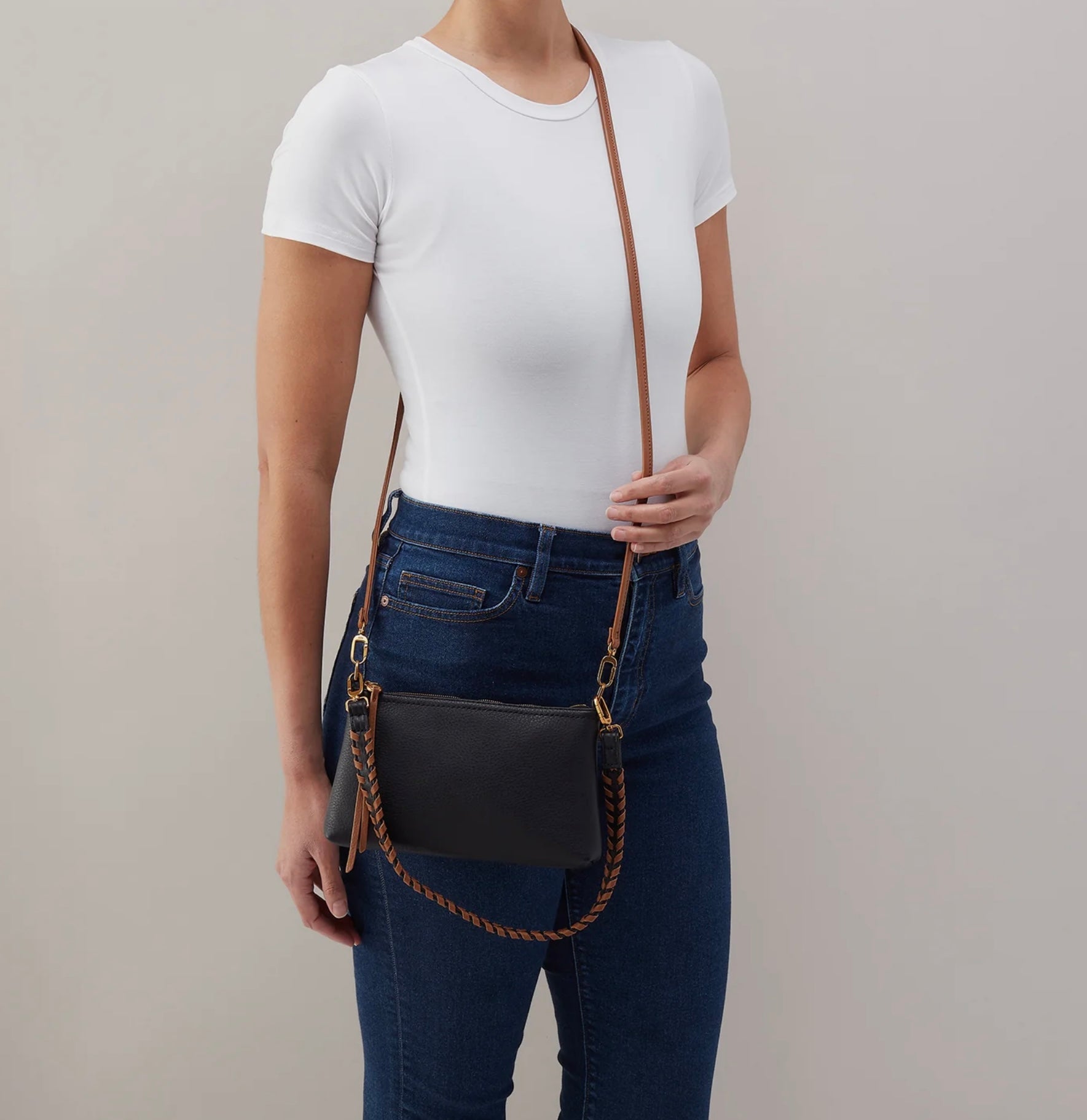 Person wearing a black crossbody bag with a brown strap on a plain background
