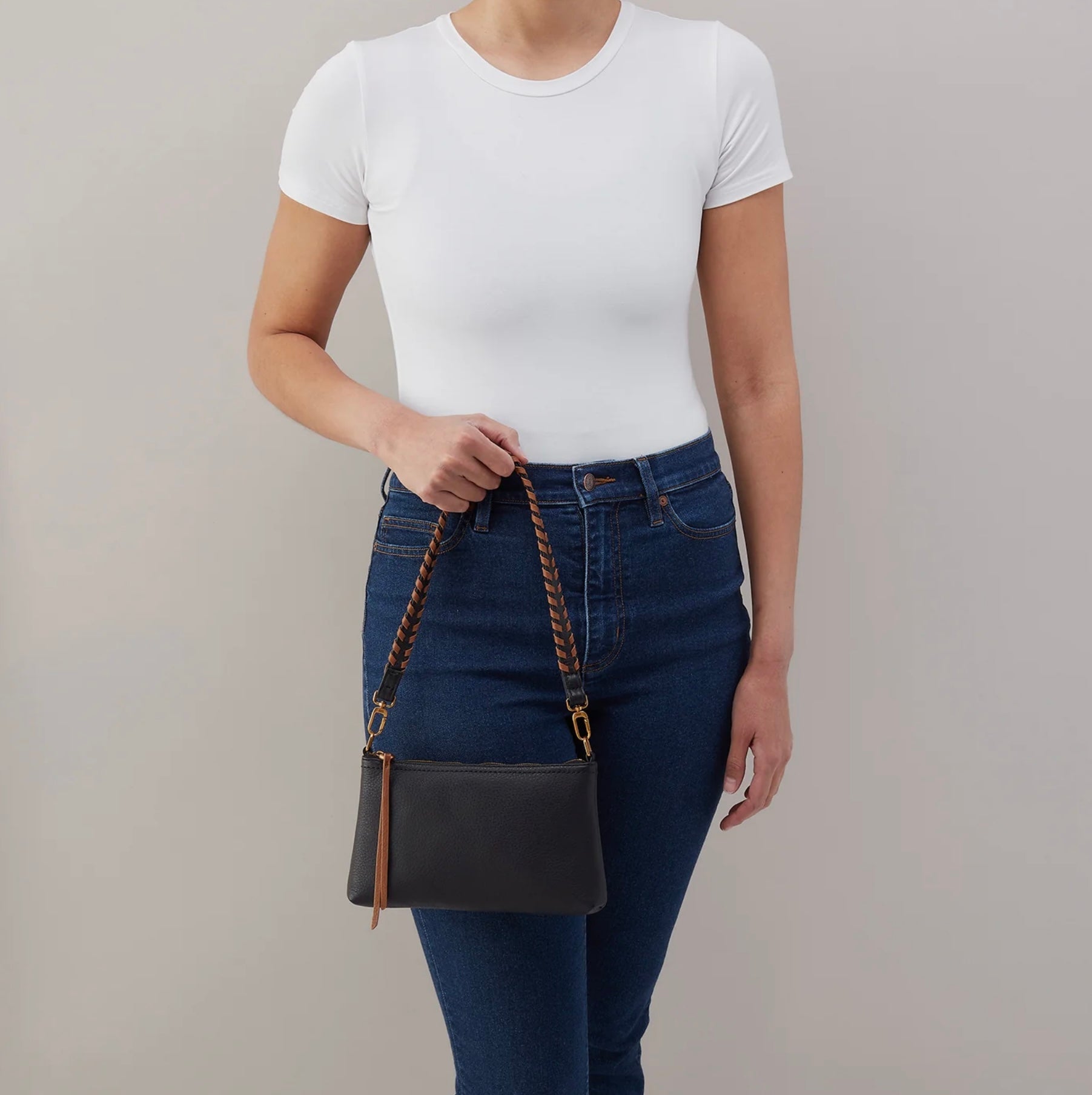 Person holding a black handbag with a brown strap against a plain background