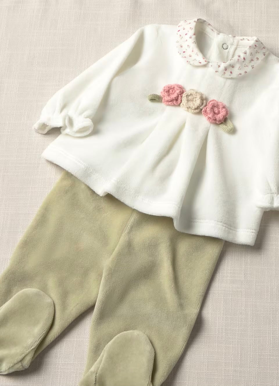 A baby girl's two-piece outfit featuring a white long-sleeve top with a floral Peter Pan collar and embroidered pink flowers on the chest, paired with sage green footed leggings, laid flat on a textured beige fabric background.