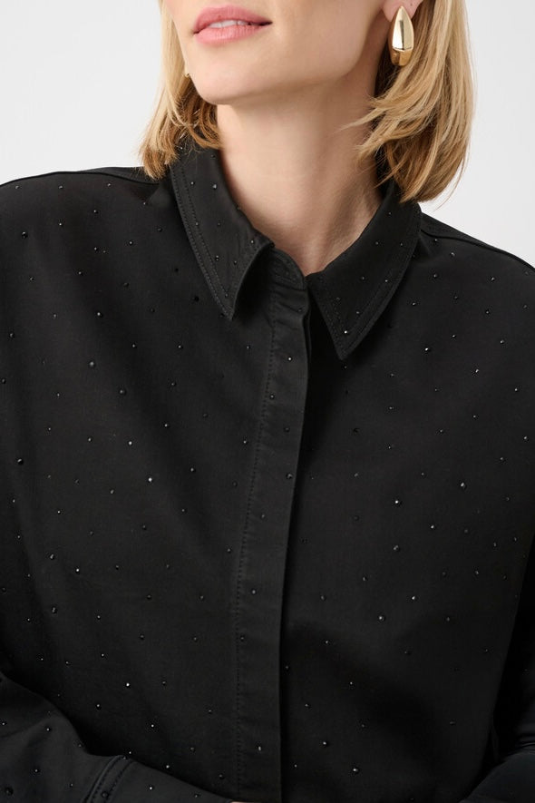 Close-up of a model wearing a black button-up shirt with a pointed collar and a subtle dotted pattern of small metallic studs or rhinestones, paired with gold hoop earrings.