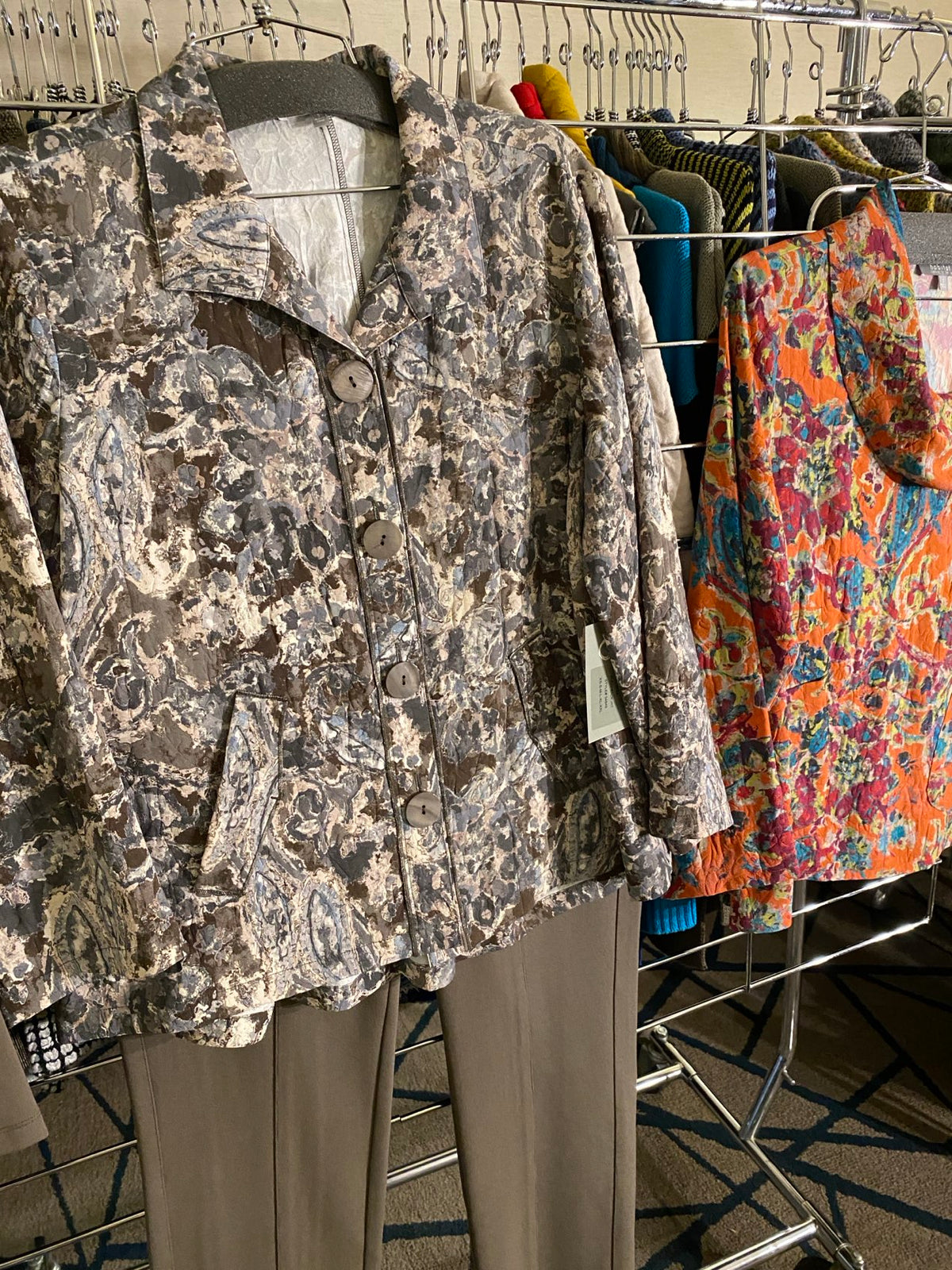 A camouflage-patterned button-front vest or jacket laid flat on a metal rack, with other folded garments visible behind it.