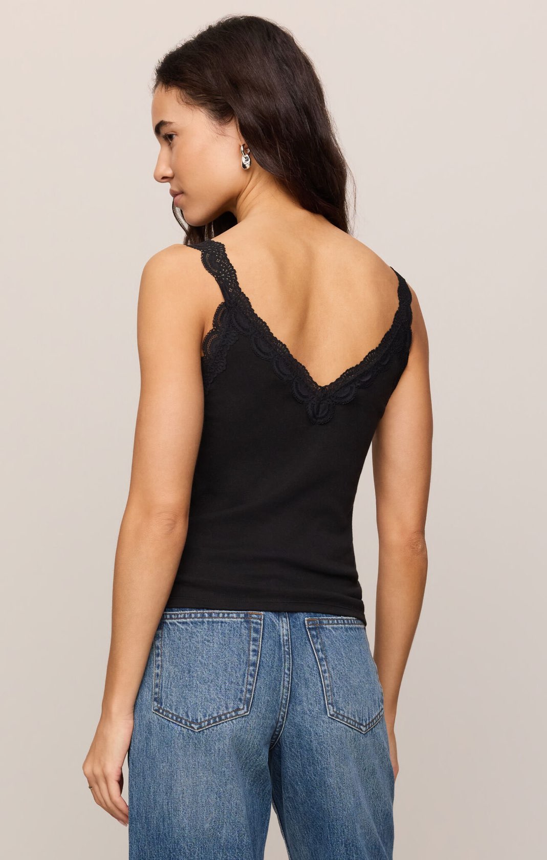 Woman wearing a black tank top and blue jeans on a beige background