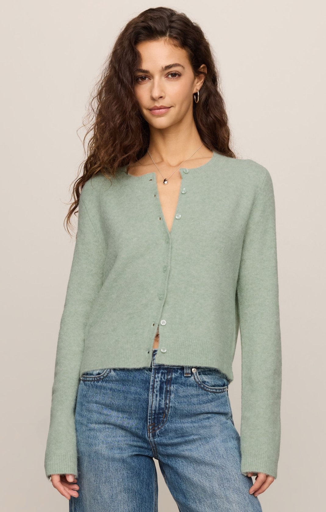 Woman wearing a light green long-sleeve shirt and blue jeans on a beige background