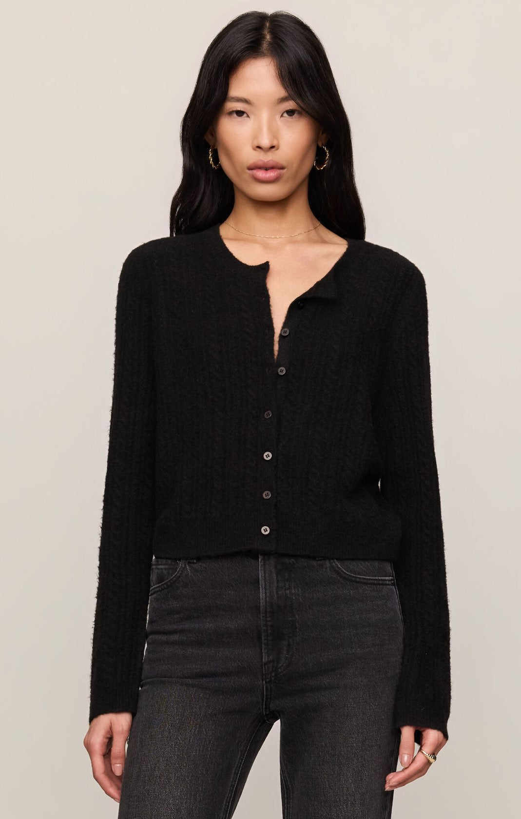 Woman wearing a black cardigan and dark jeans against a plain background