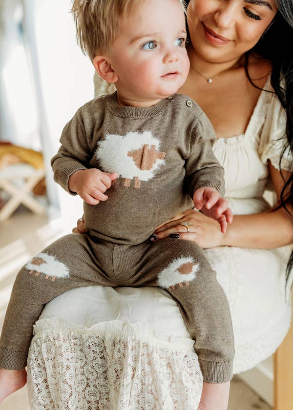 Baby wearing a brown outfit with white patches, sitting on a woman's lap.